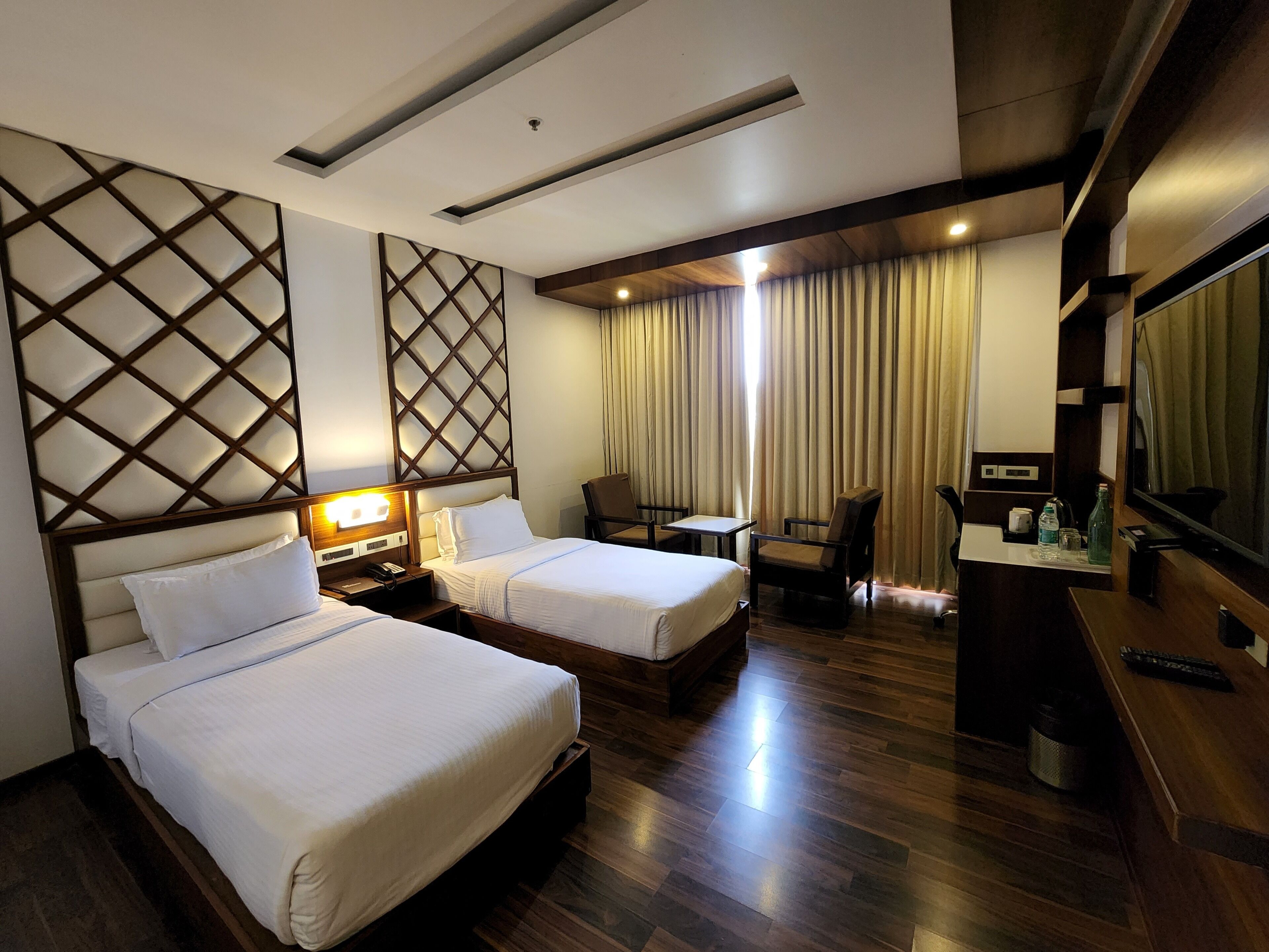 A hotel room with two beds, a desk, a chair, a TV, and a mirror.