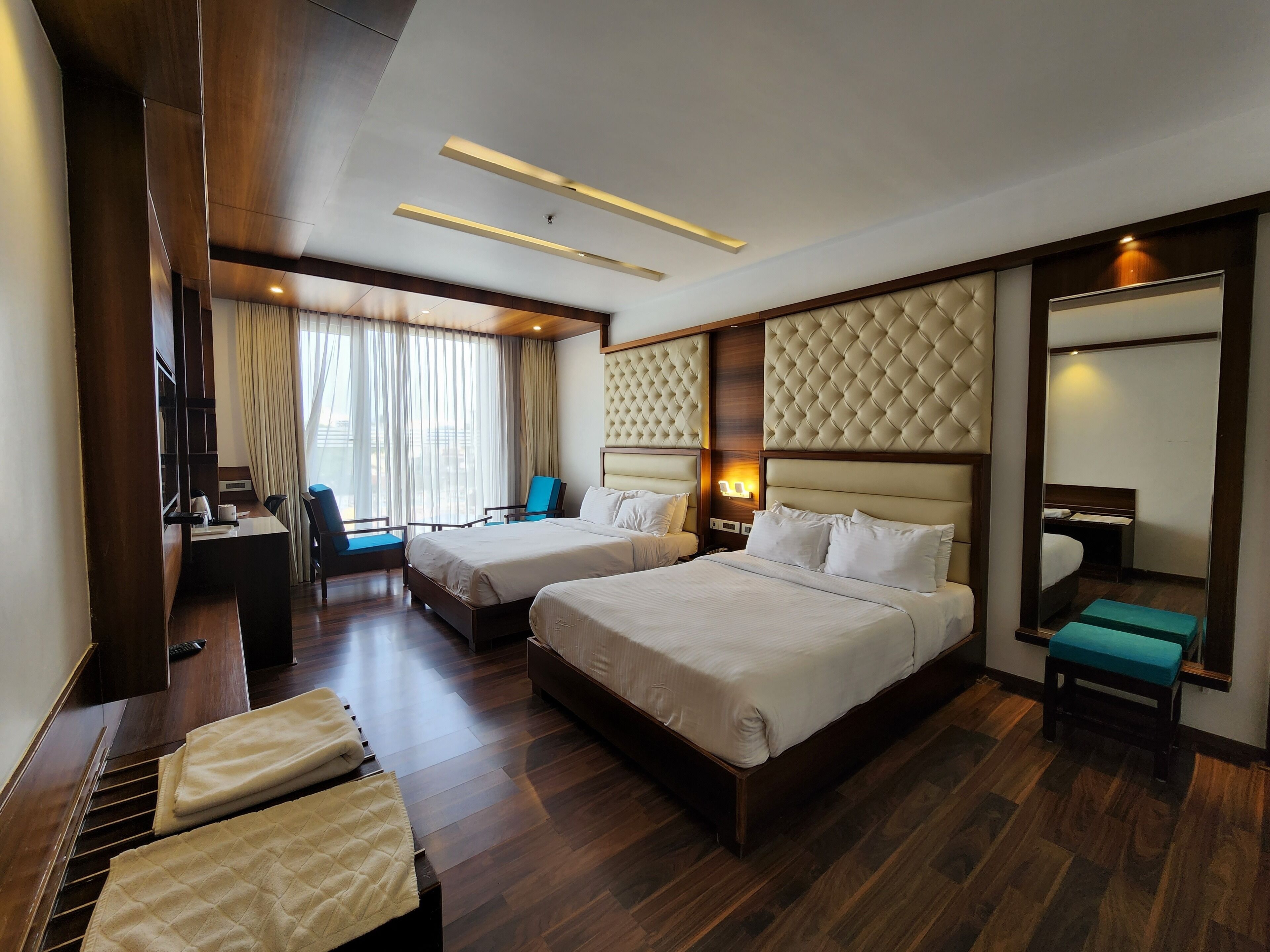 Habitación de hotel con dos camas, un escritorio con silla, un espejo y una ventana con cortinas.