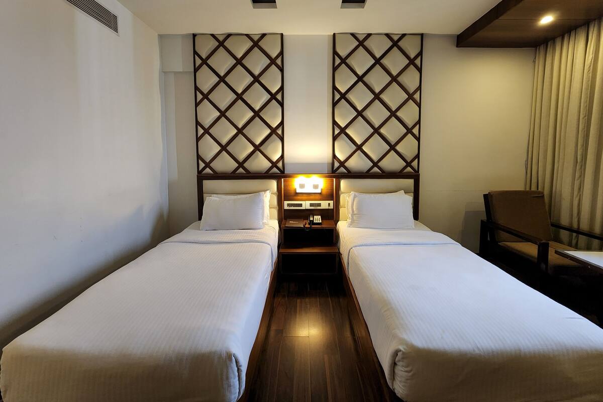 A hotel room with two single beds, a nightstand with a lamp, a chair, and a decorative wall panel.