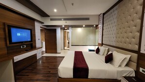 A modern bedroom with a large bed, wooden flooring, a TV on the left wall, and a sliding door leading to a bathroom. - Hotel Preethi International (Mysore)