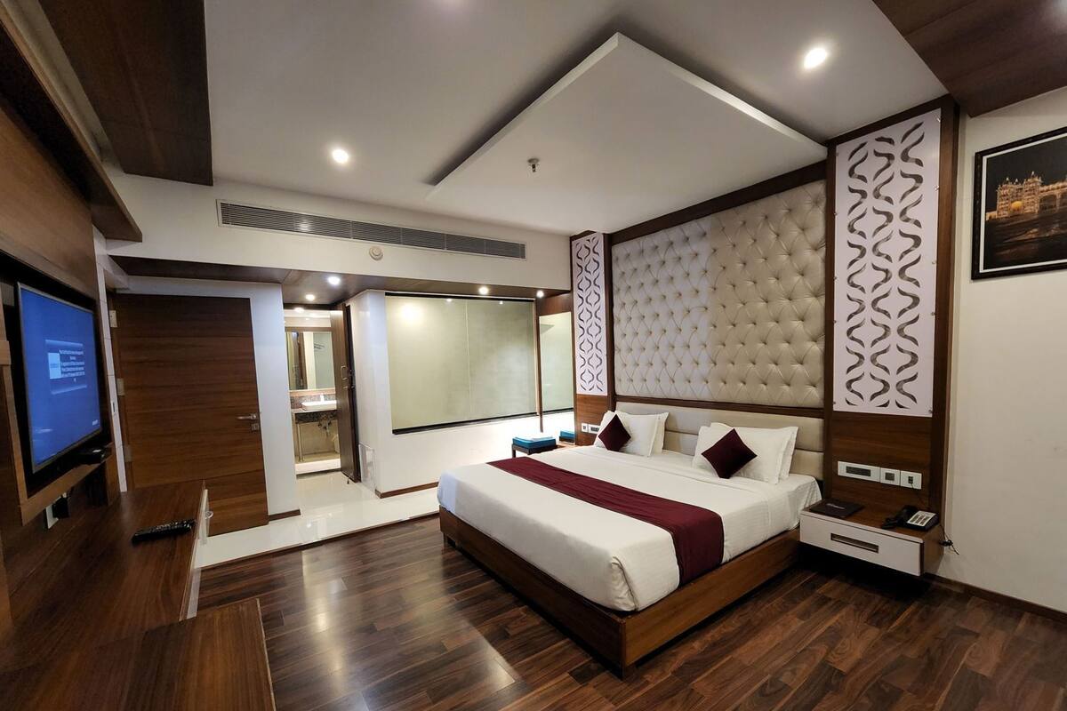 A modern hotel room with a large bed, a television, a desk, and a bathroom visible through an open door.