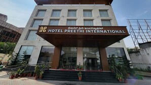 The exterior of Hotel Preethi International with a modern facade, large windows, and a prominent entrance with steps and potted plants. - Hotel Preethi International (Mysore)