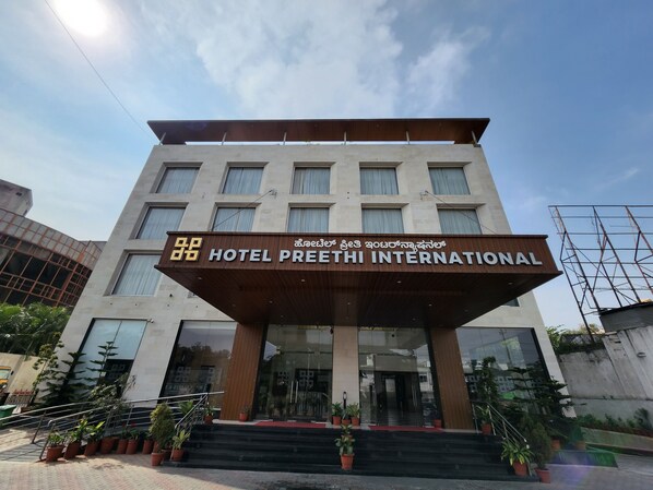 The exterior of Hotel Preethi International with a modern facade, large windows, and a prominent entrance with steps and potted plants.