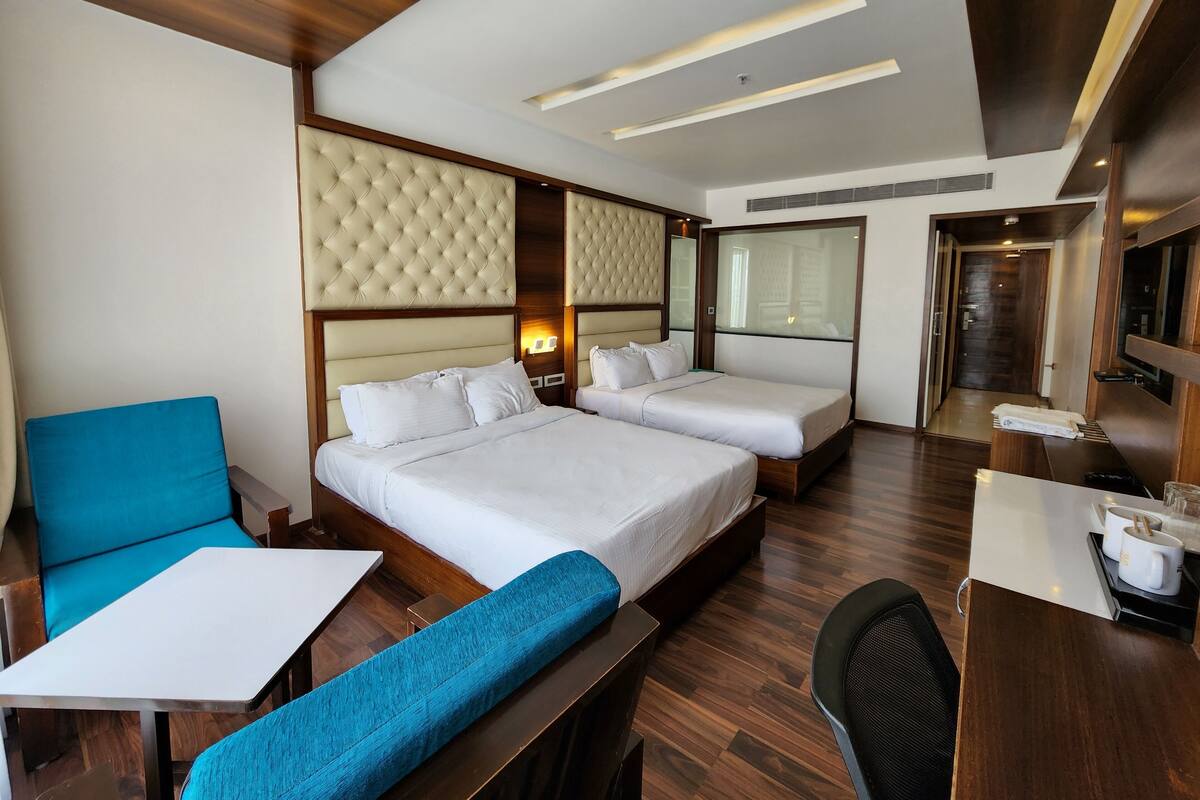 A hotel room with two beds, a desk, a chair, and a sofa.