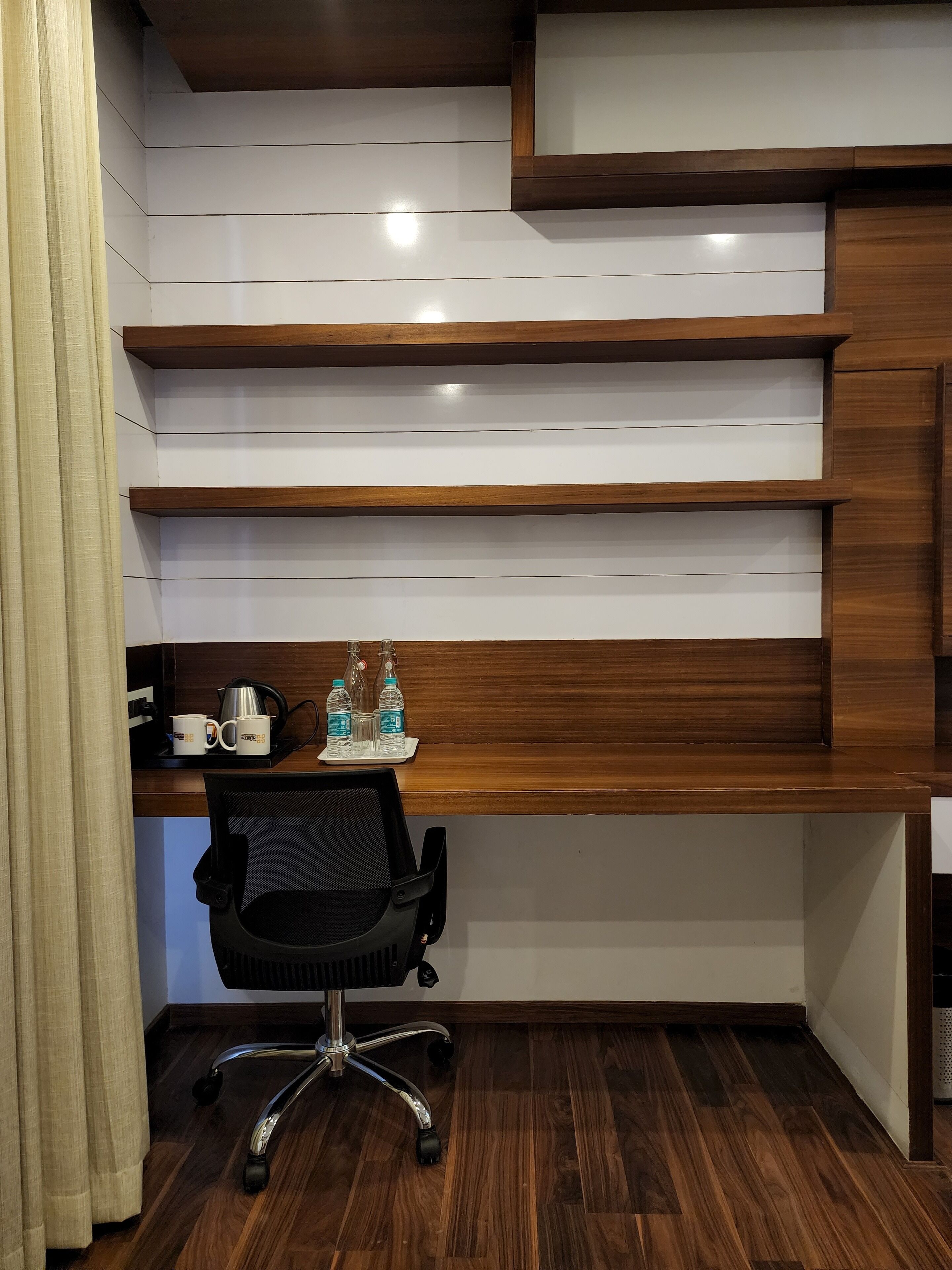 Ein moderner Arbeitsplatz mit Schreibtisch aus Holz, schwarzem Bürostuhl und Kaffeemaschine.