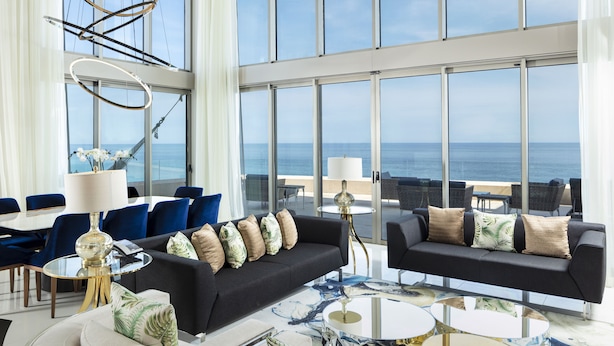 A modern hotel lobby with a large ocean view, featuring a black sofa, blue chairs, and a glass coffee table. - Garza Blanca Los Cabos - All Inclusive (Cabo San Lucas)