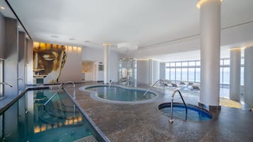 Una piscina interior moderna con agua cristalina, rodeada de grandes pilares y un mural de un rostro en la pared.