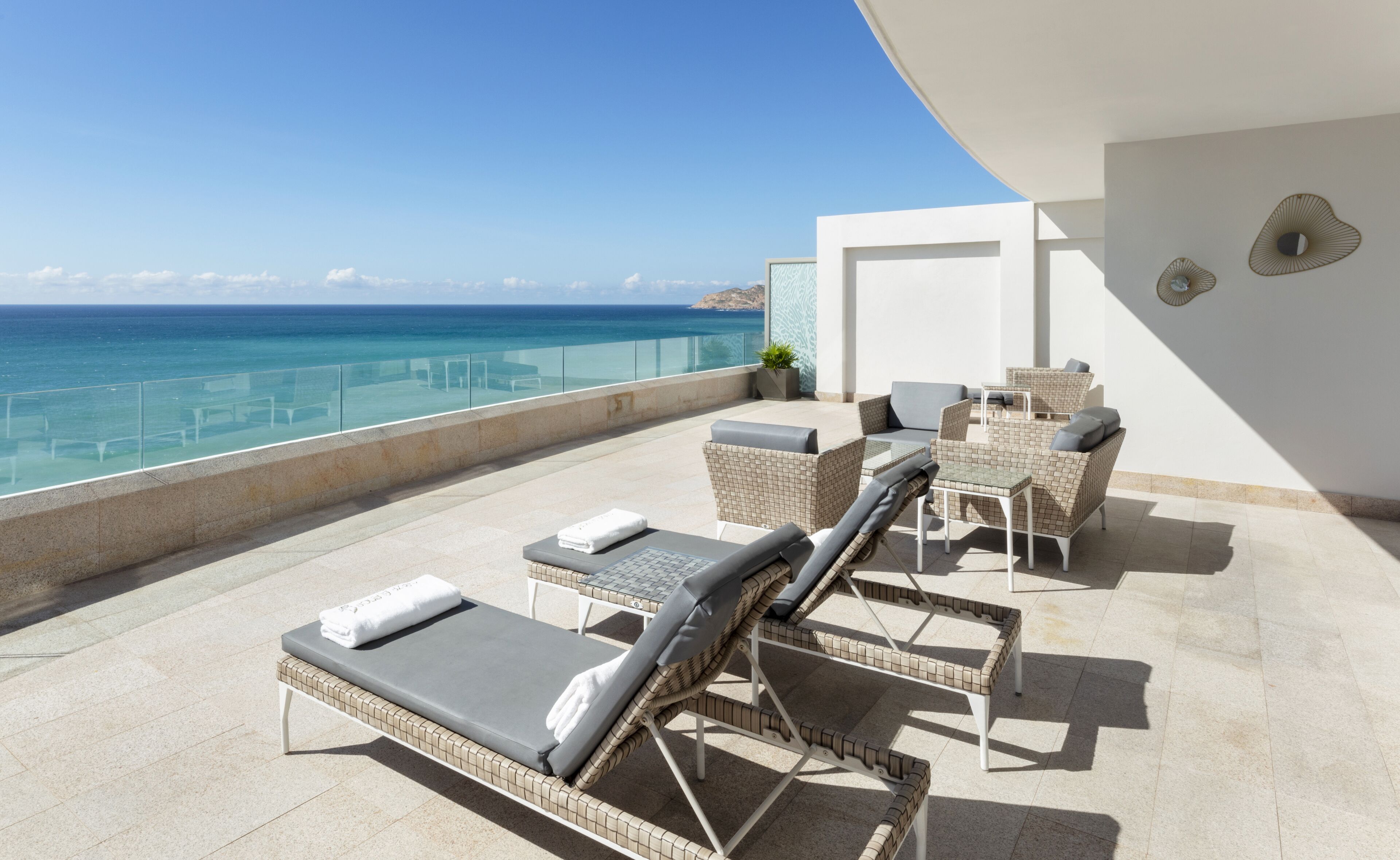 Un espace extérieur ensoleillé, aménagé avec des fauteuils confortables et une table, offrant une vue imprenable sur une mer d’un bleu profond.