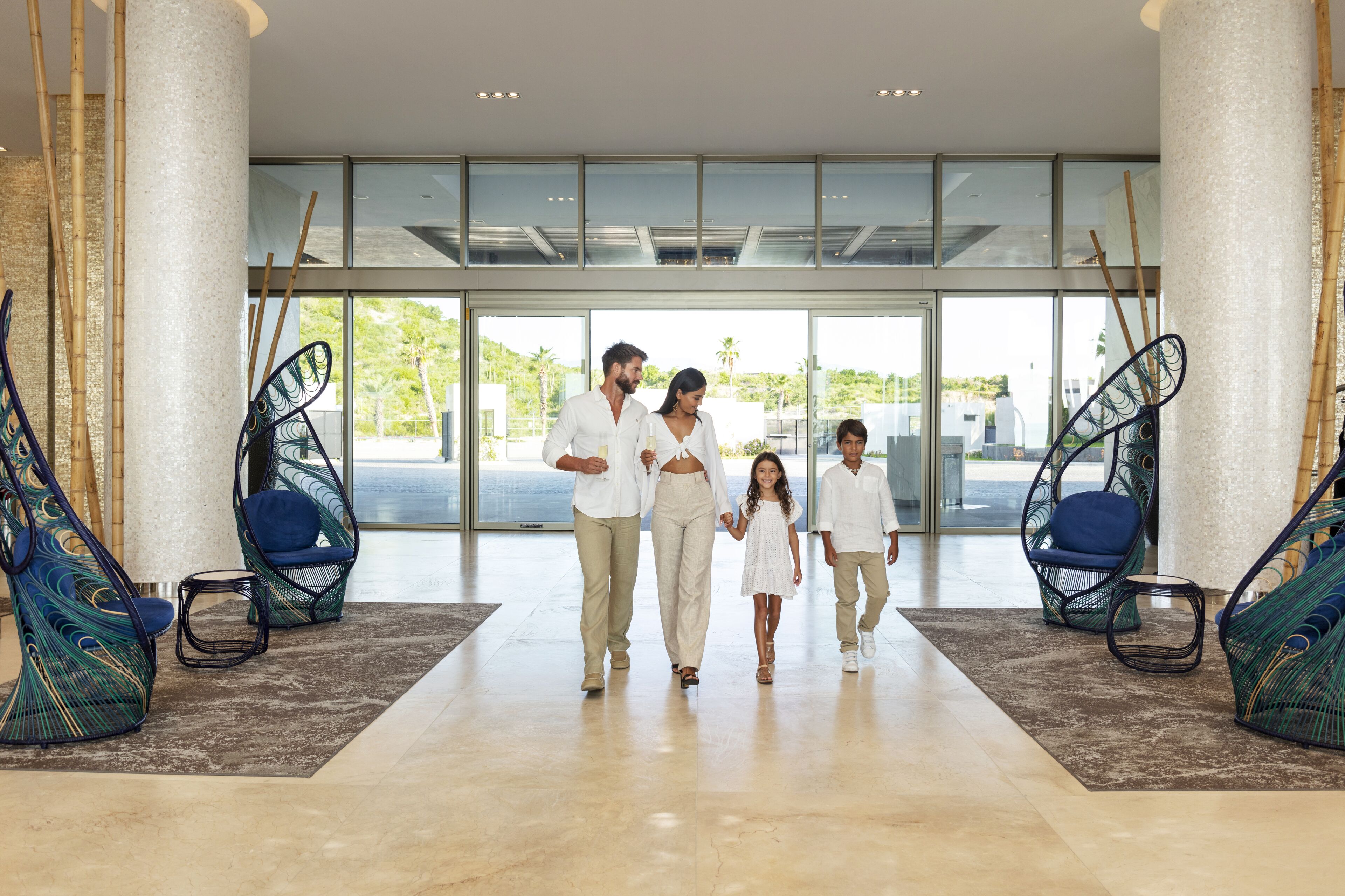 Een gezin loopt door een moderne lobby met glazen deuren, stoelen met pauwenprint en een marmeren vloer.