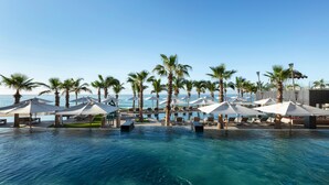A pool area with lounge chairs and umbrellas, palm trees, and a view of the ocean. - Garza Blanca Los Cabos - All Inclusive (Cabo San Lucas)