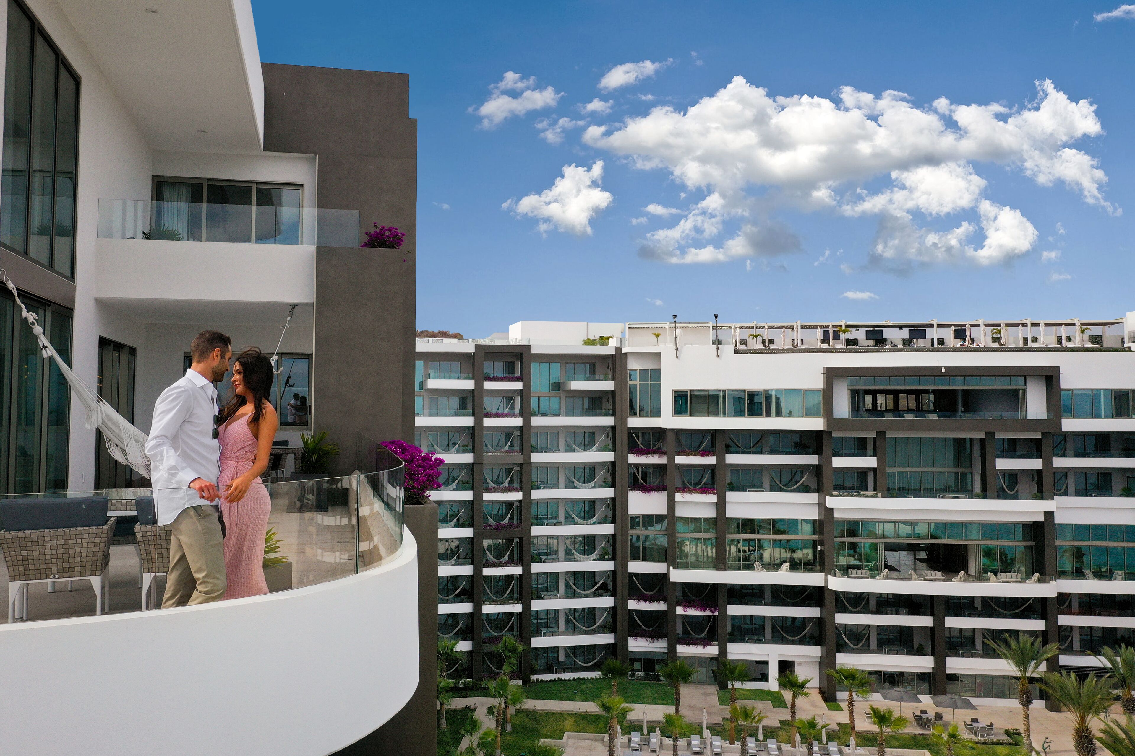 Un hotel moderno con balcón, mobiliario exterior y vistas de los edificios circundantes.