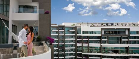 Un hotel moderno con balcón, mobiliario exterior y vistas de los edificios circundantes.