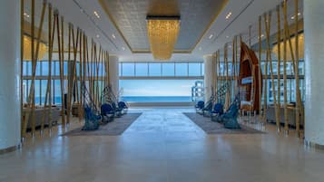 A spacious lobby with a view of the ocean, featuring a modern chandelier, bamboo columns, and seating areas.