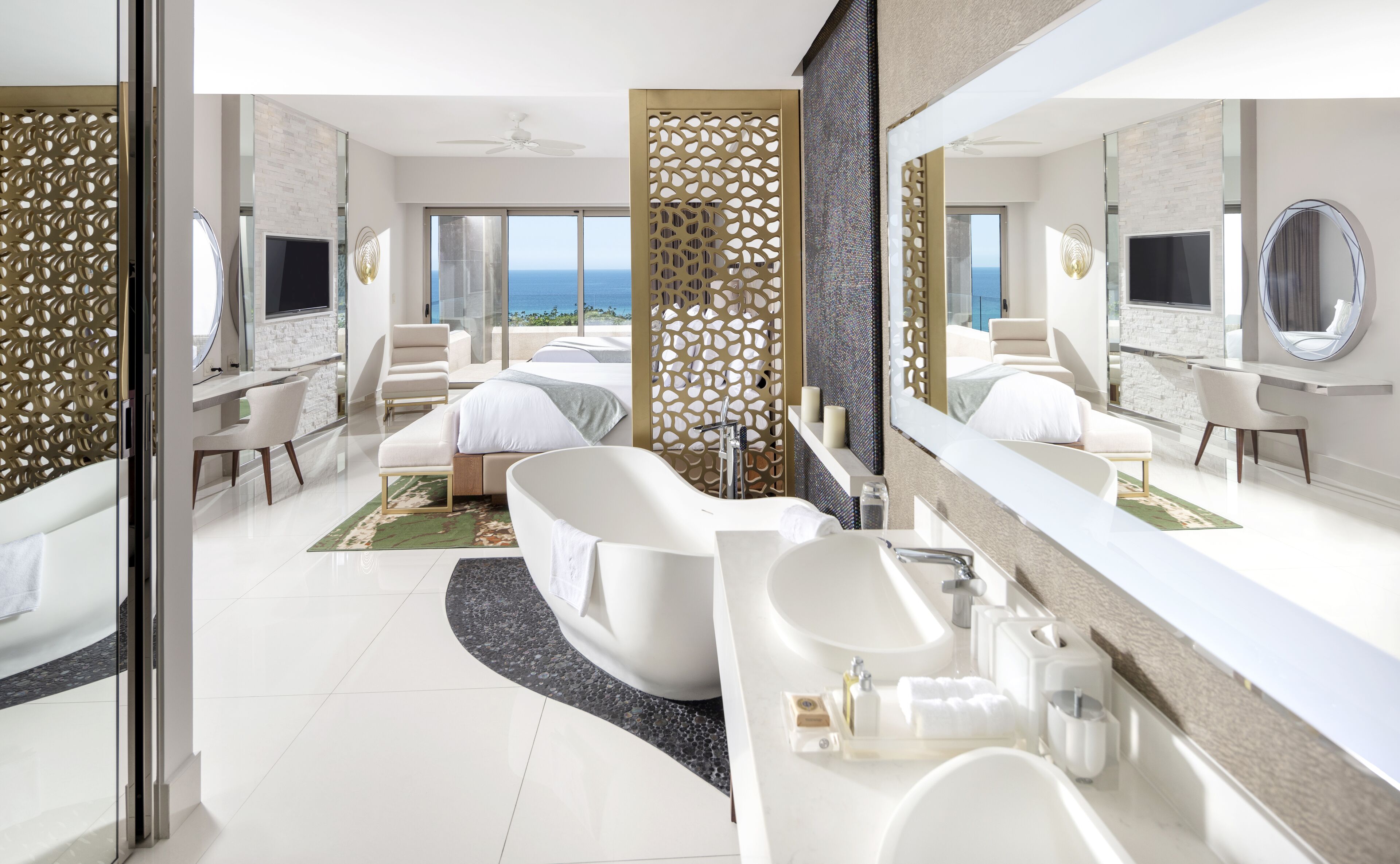 A modern hotel room with a large bed, a bathtub, a vanity with a mirror, and a view of the ocean.