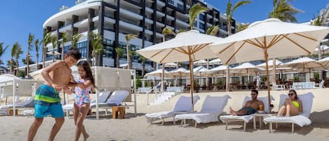A beach area with lounge chairs and umbrellas, a building in the background, and a text overlay stating "UP TO 2 KIDS STAY FREE".