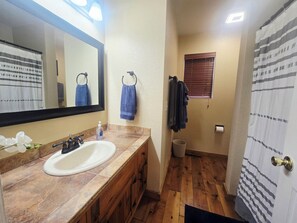 A bathroom with a sink, mirror, wooden cabinets, a towel rack, a window, and a shower curtain. - Quiet retreat (Pinetop)