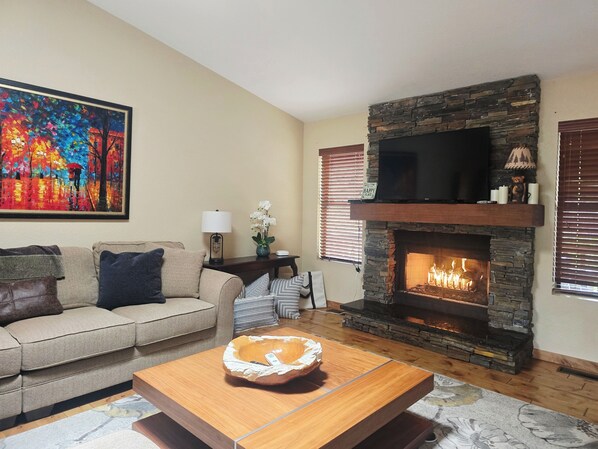 A living room with a stone fireplace, a sofa, a coffee table, and a painting on the wall.