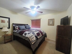 A bedroom with a bed, a ceiling fan, a bedside table with a lamp, a window with blinds, a TV on a stand, and a dresser. - Quiet retreat (Pinetop)