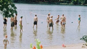 Un groupe de personnes jouant au volleyball dans un lac, entouré d’arbres.