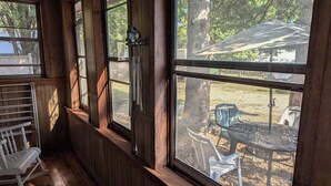 Un intérieur en bois avec de grandes fenêtres, un fauteuil à bascule blanc et une vue sur l’espace extérieur aménagé pour s’asseoir.
