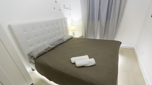 Un letto rifatto con una coperta marrone e due asciugamani bianchi piegati, una testata bianca, una lampada da comodino e una parete decorata con adesivi a forma di uccelli.