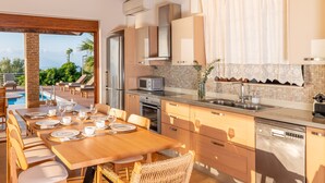 A modern kitchen with a dining area, a view of the pool, and a view of the mountains. - Iris Villas Lefkada - Karavi Villa (Lefkada)