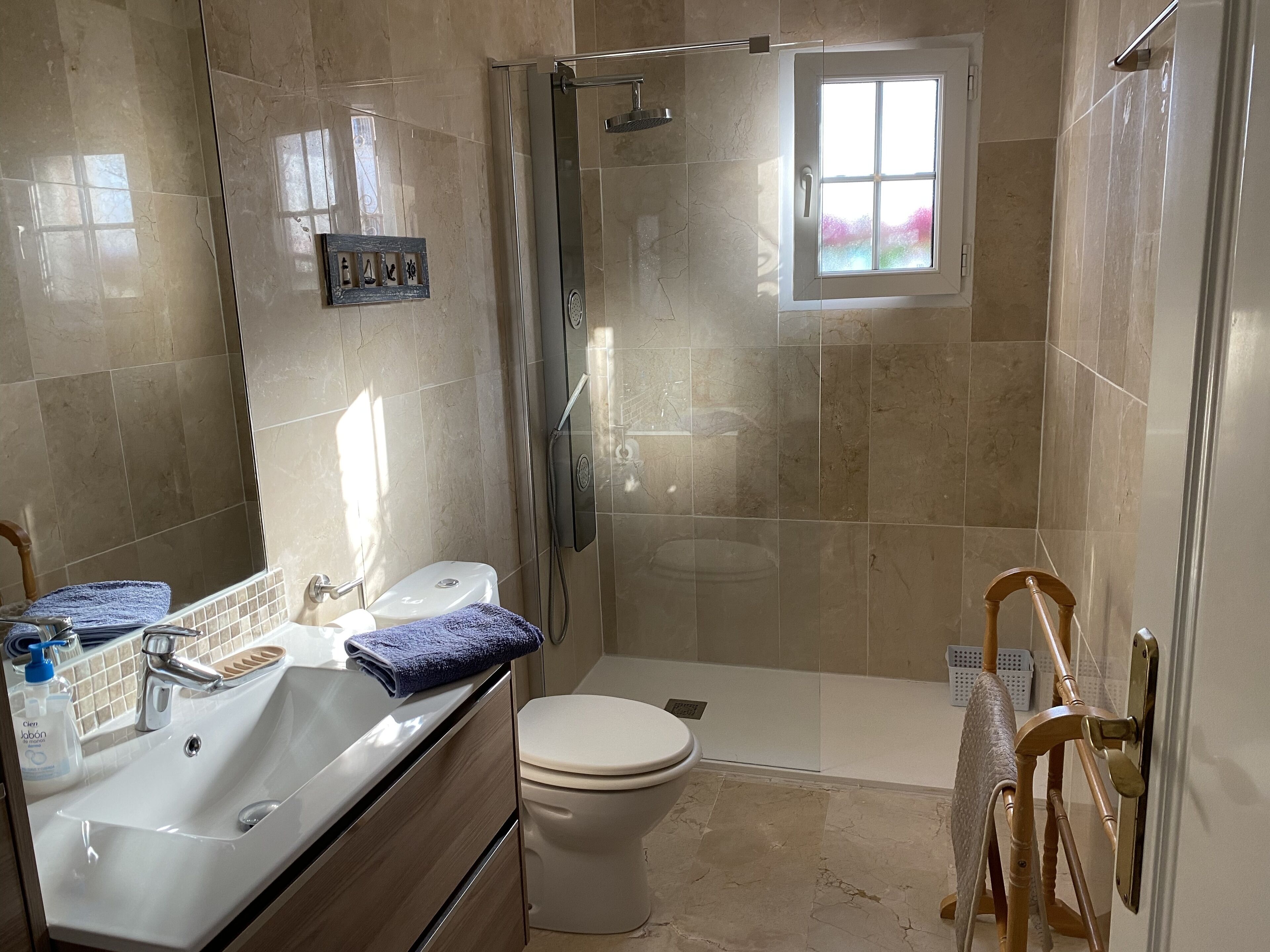 A bathroom with a shower, toilet, sink, and a small window.