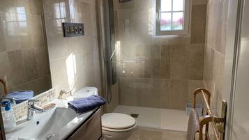 A bathroom with a shower, toilet, sink, and a small window.