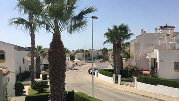 A residential street with palm trees, white houses, and a clear sky.