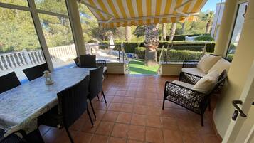 A covered patio area with a dining table and chairs, a sofa, and a view of a landscaped garden.