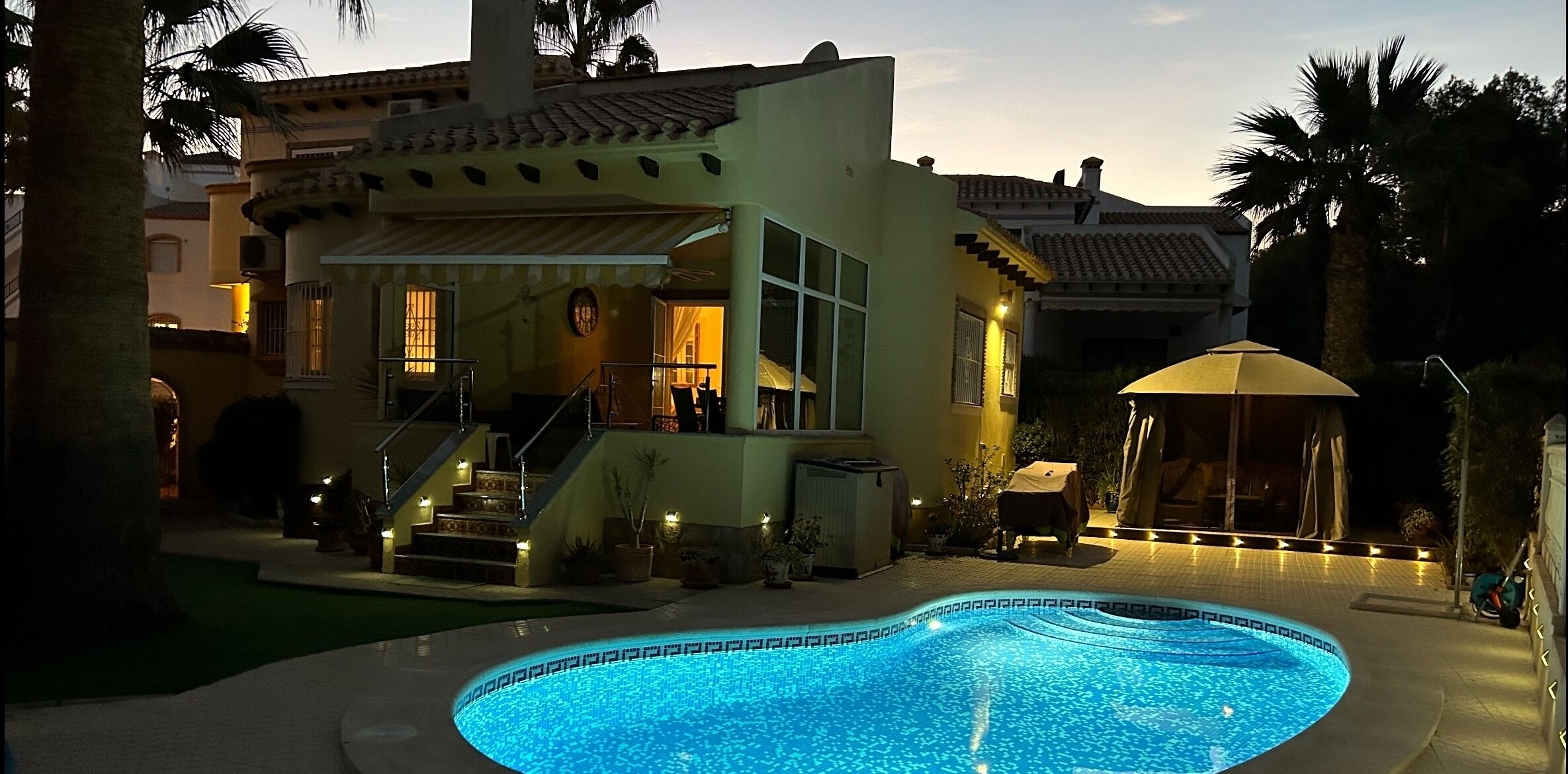 A poolside area with a swimming pool, a covered seating area, and a staircase leading to a second-story balcony.