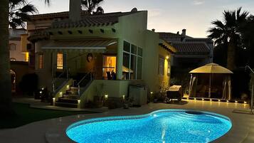 A poolside area with a swimming pool, a covered seating area, and a staircase leading to a second-story balcony.