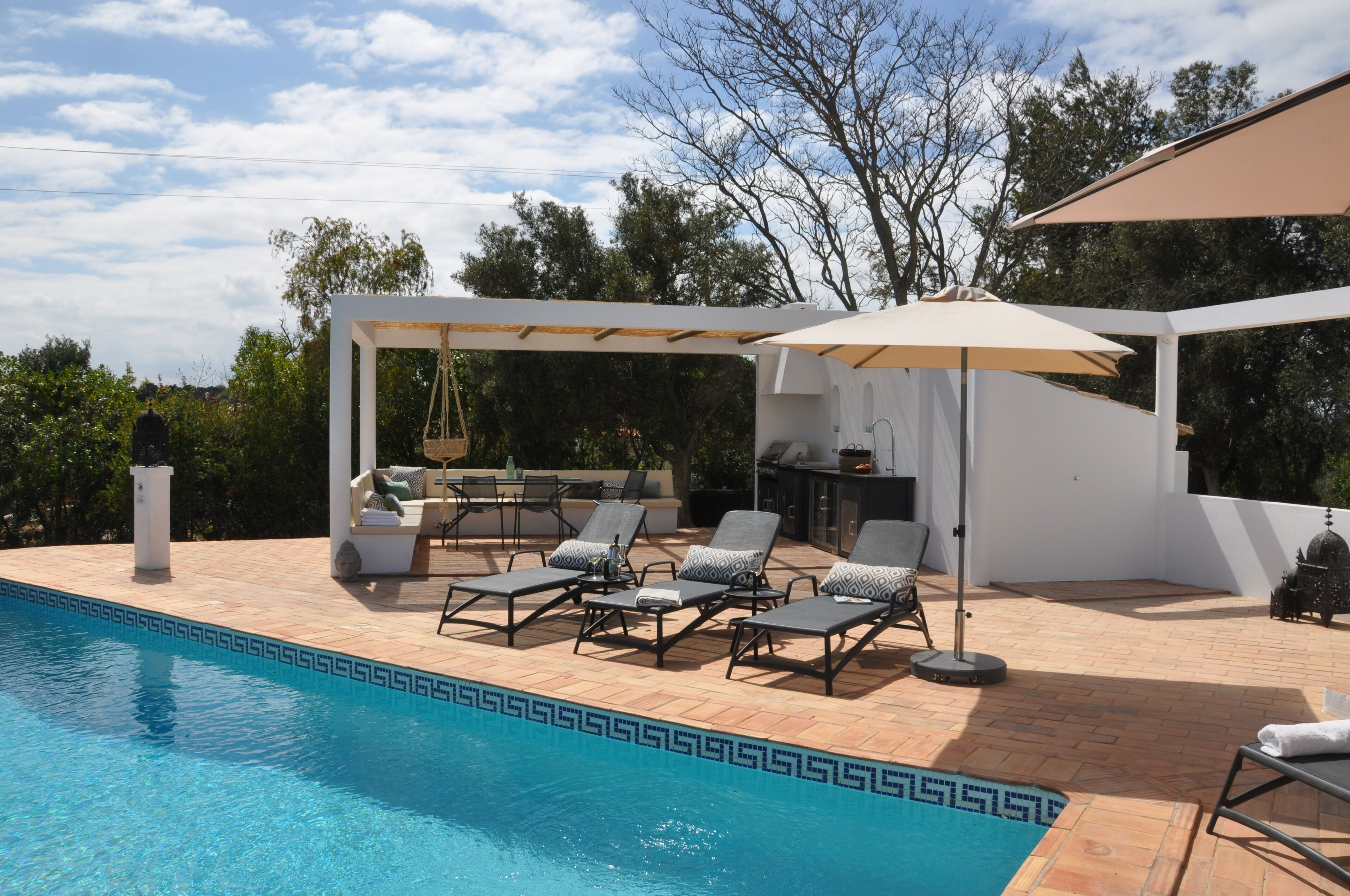 A poolside area with lounge chairs, a pergola, and a barbecue setup.