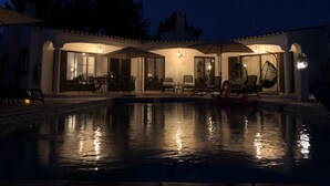 Una piscina con lettini e ombrelloni, circondata da un edificio con ampie finestre e porte.