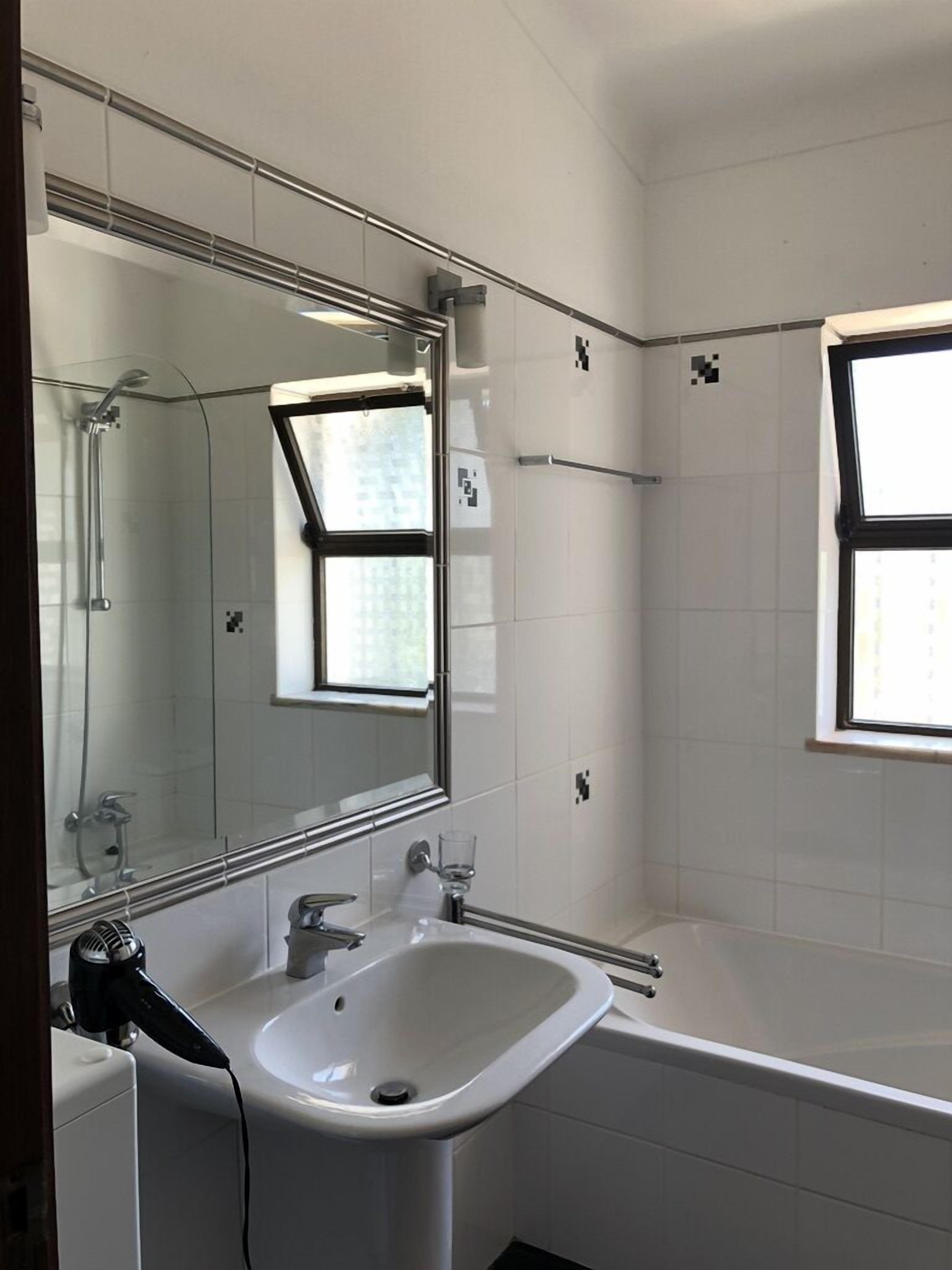 A modern bathroom with a large mirror, a sink, a shower, and a window.