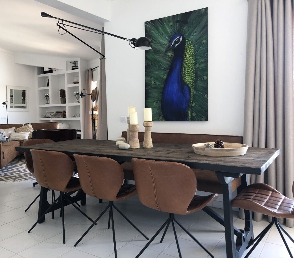 A dining area with a wooden table, brown chairs, and a peacock painting on the wall.