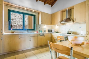 A modern kitchen with wooden cabinets, a stone-framed window, a microwave, and a sink. - Villa Ventura - Three Bedroom Villa, Sleeps 6 (Skala)
