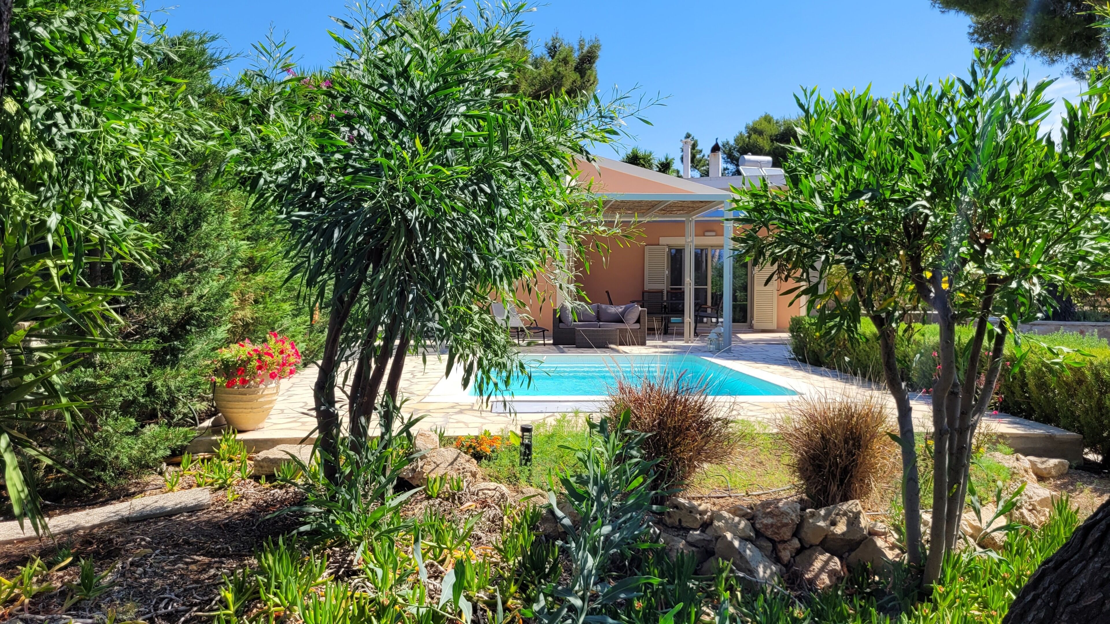 Ein Poolbereich mit einem modernen Haus im Hintergrund, umgeben von üppiger Vegetation und einer Steinmauer.