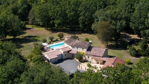 A large house with a swimming pool, surrounded by dense trees and a well-maintained lawn.