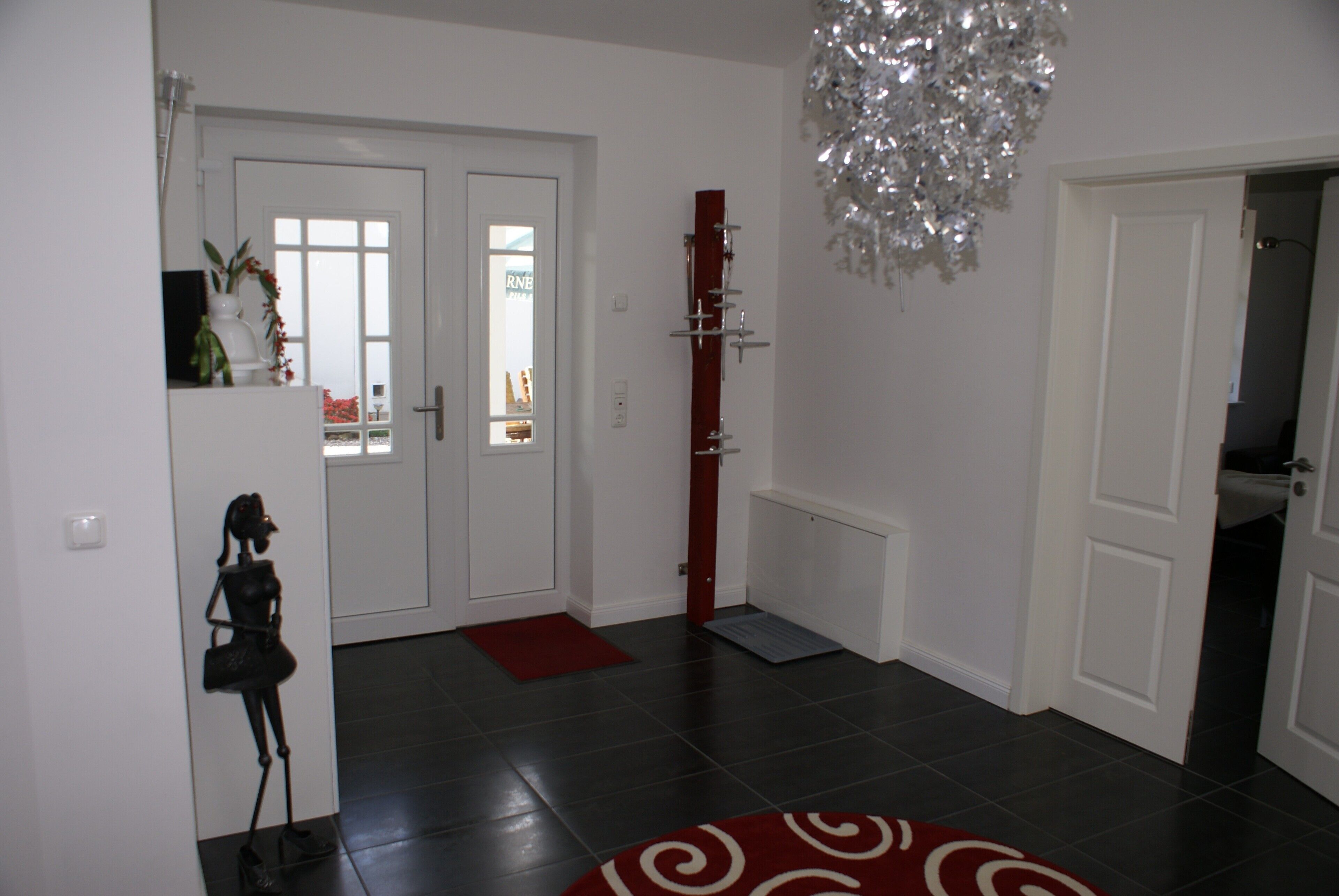 A hallway with a red carpet, white doors, a decorative metal sculpture, and a chandelier.