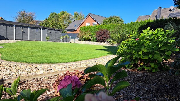 A well-maintained backyard with a lawn, a stone pathway, and various plants and flowers. - House, superior equipment, city limits Rostock, pets welcome, internet (Groß Kussewitz)