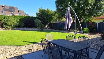 En terrasse med et bord og stole, omgivet af en velplejet græsplæne og en kant af sten.