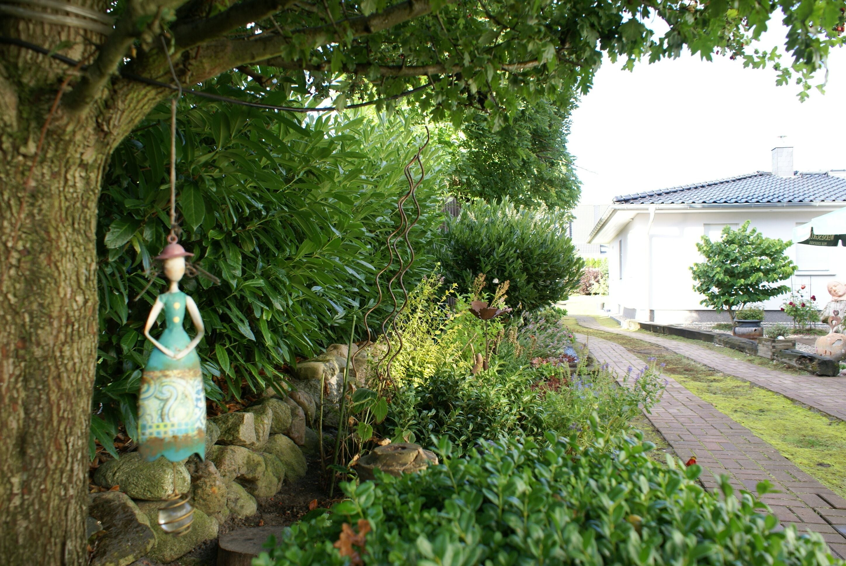 Ein Garten mit einer Statue, einem Baum und einem Weg, der zu einem Gebäude führt.