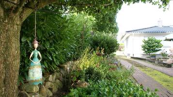 Ein Garten mit einer Statue, einem Baum und einem Weg, der zu einem Gebäude führt.