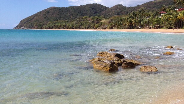 A beach with clear shallow waters, rocky outcrops, and a distant mountain range. - OCEAN VIEW VILLA WITH PRIVATE POOL, STEPS FROM SECLUDED BEACH, GATED COMMUNITY! (Yabucoa)