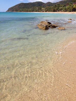 A beach with clear shallow waters, rocky outcrops, and a distant mountain range. - OCEAN VIEW VILLA WITH PRIVATE POOL, STEPS FROM SECLUDED BEACH, GATED COMMUNITY! (Yabucoa)