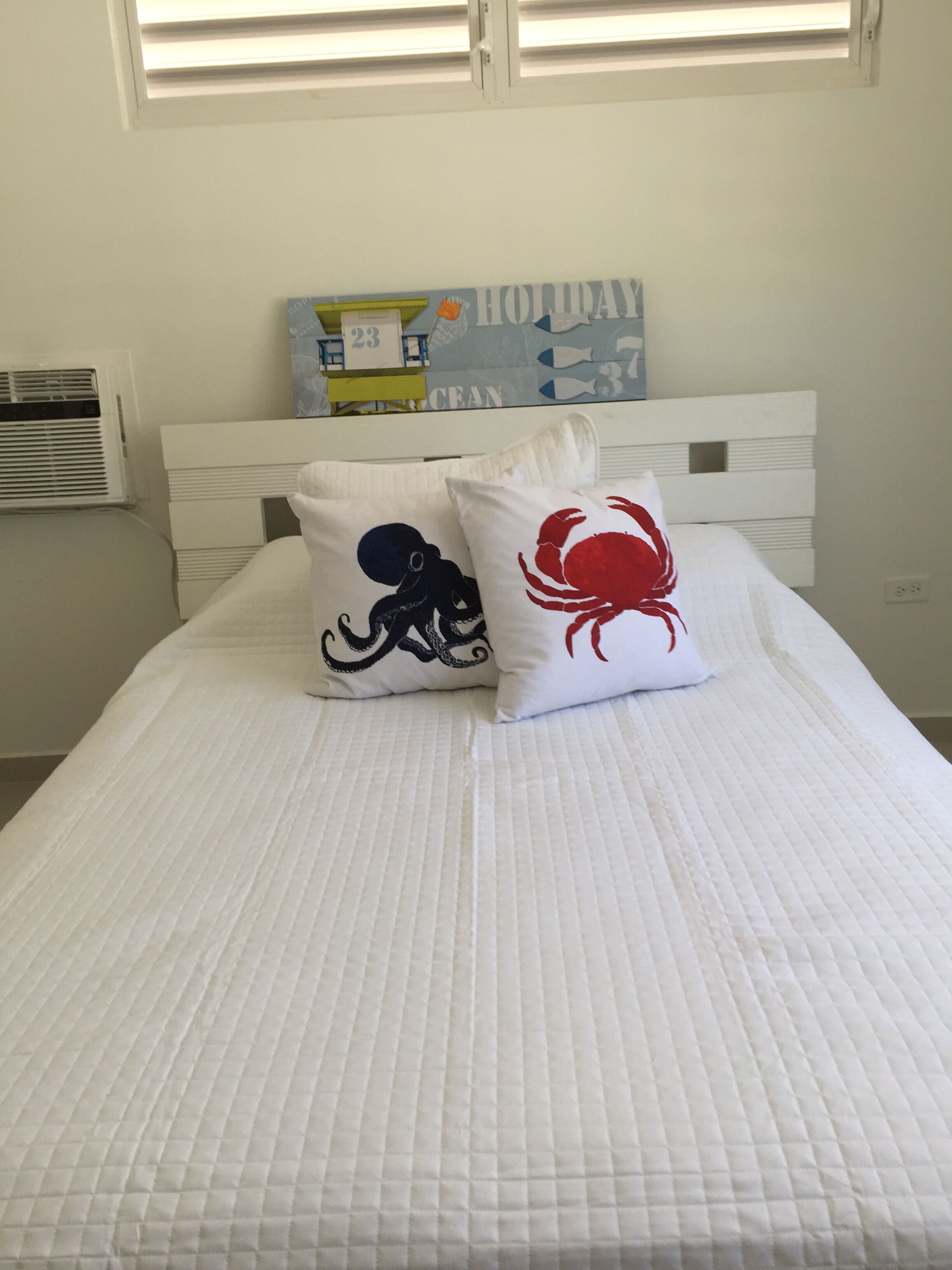 Een bed met twee kussens, waarvan één een octopus dessin heeft en de ander een krab, met een wanddecoratie erboven.