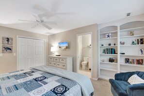 A bedroom with a bed, a dresser, a nightstand, a ceiling fan, a bookshelf, and a bathroom visible through an open door. - SeaPines, Ranch style home, Nicely updated, Great outdoor space, Pet friendly (hilton head)