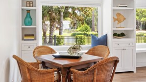A dining area with wicker chairs, a wooden table, and a view of a garden through a window. - 63 South Sea Pines: A BESTNEST by Beverly Serral (Hilton Head Island)
