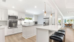A modern kitchen with white cabinetry, stainless steel appliances, and a central island with bar stools. - 63 South Sea Pines: A BESTNEST by Beverly Serral (Hilton Head Island)
